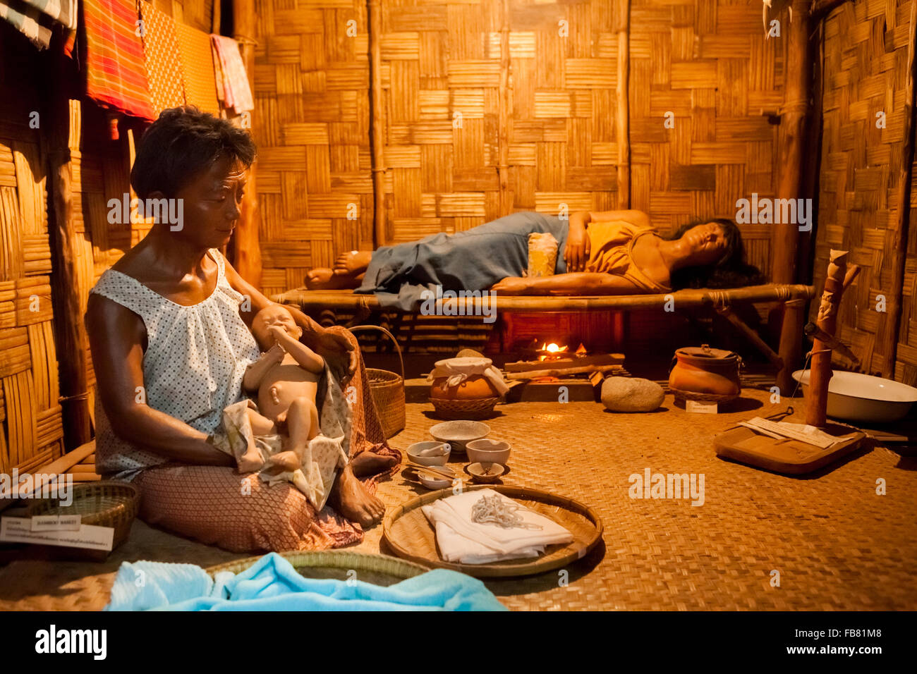 Life-size diorama with scene of childbirth. The mother lies with firebox below bamboo bed to keep her warm. Stock Photo