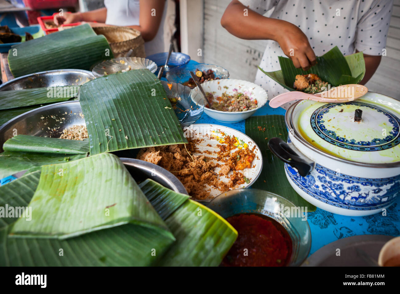 A woman serving customers at a street-side food vendor offering traditionally cooked food in Klungkung, Bali, Indonesia. Stock Photo