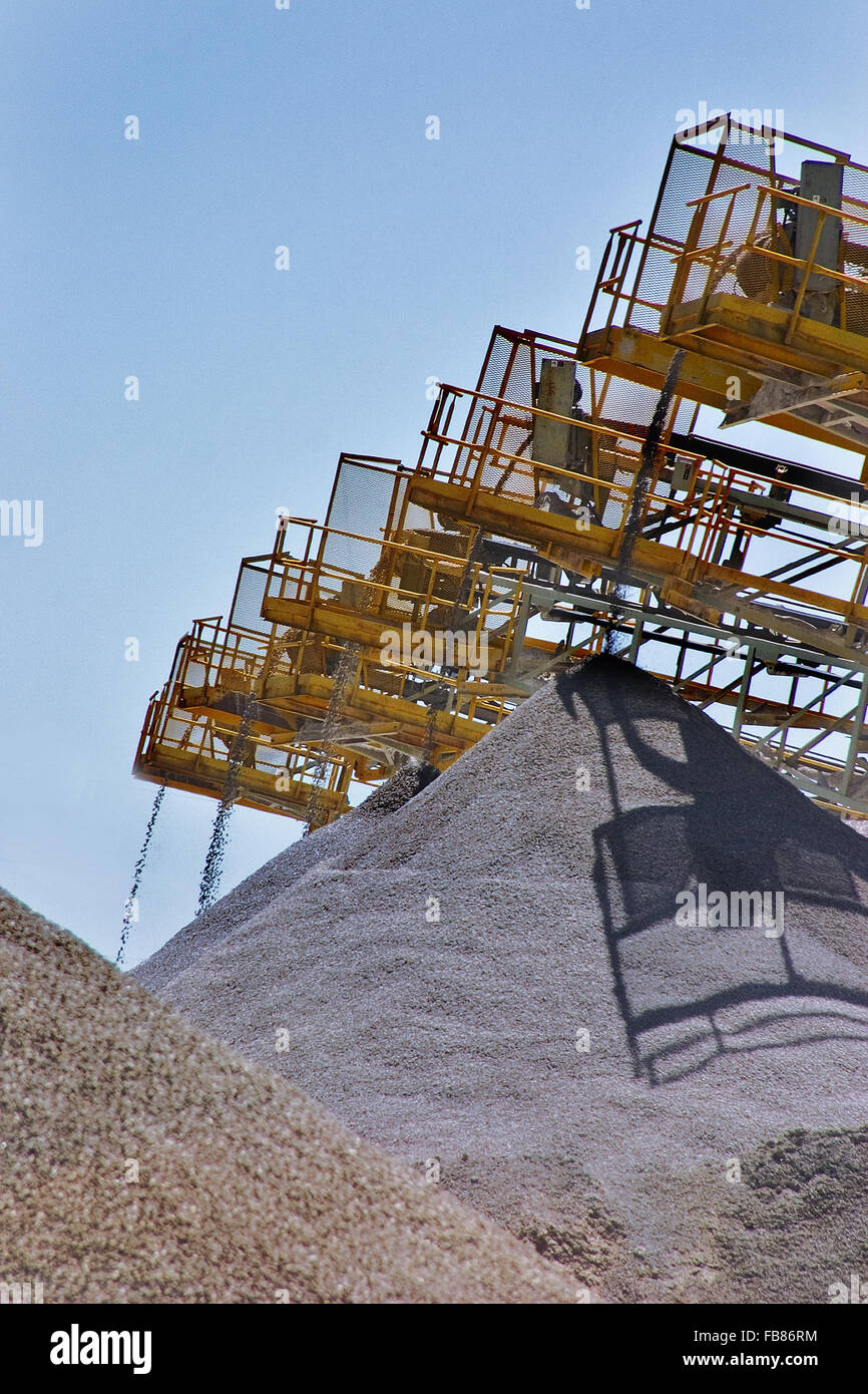 Crushed stone is sized then falls into piles from conveyor belts after being processed at a rock quarry. Stock Photo