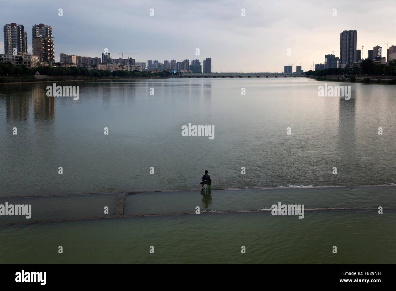 A angler sits in the middle of the Mianyuan River in Deyang city in Sichuan while angling for fish in dammed section of river. Stock Photo