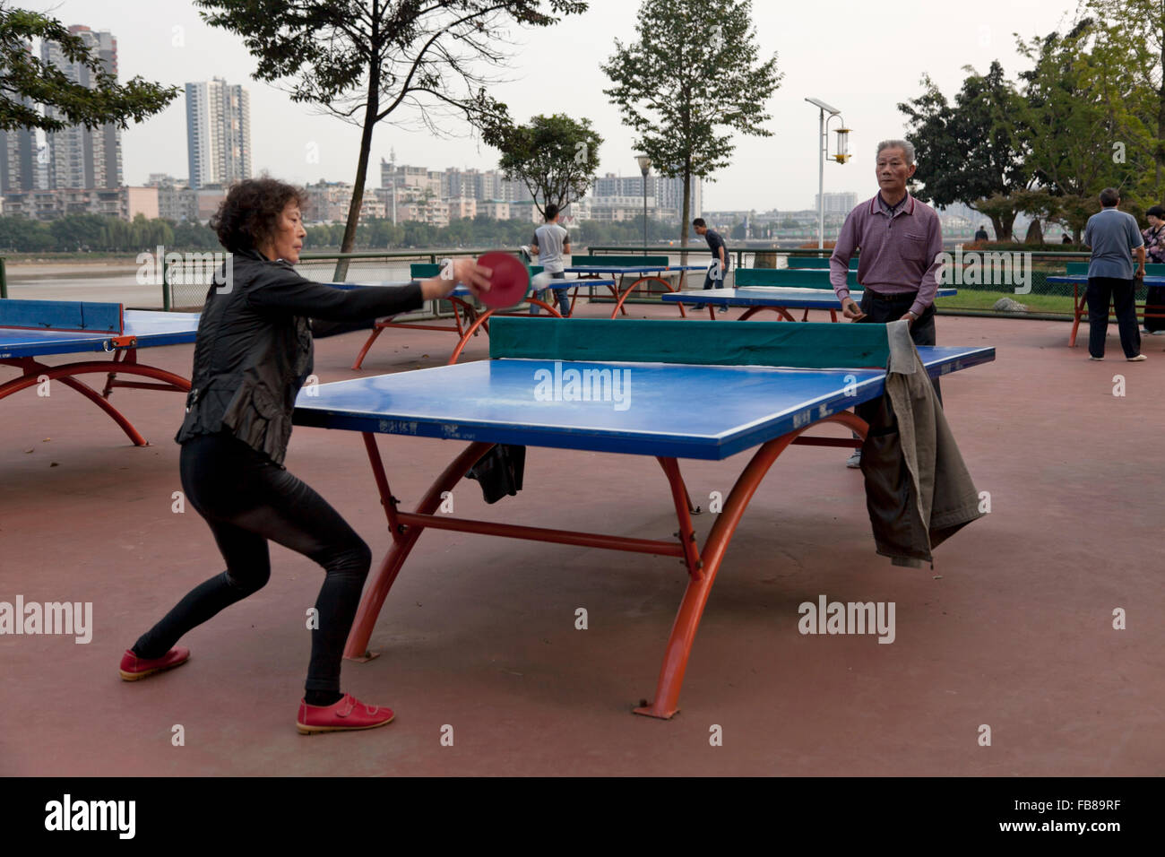 People play table tennis at a park on the riverfront at a typical city in China. Stock Photo