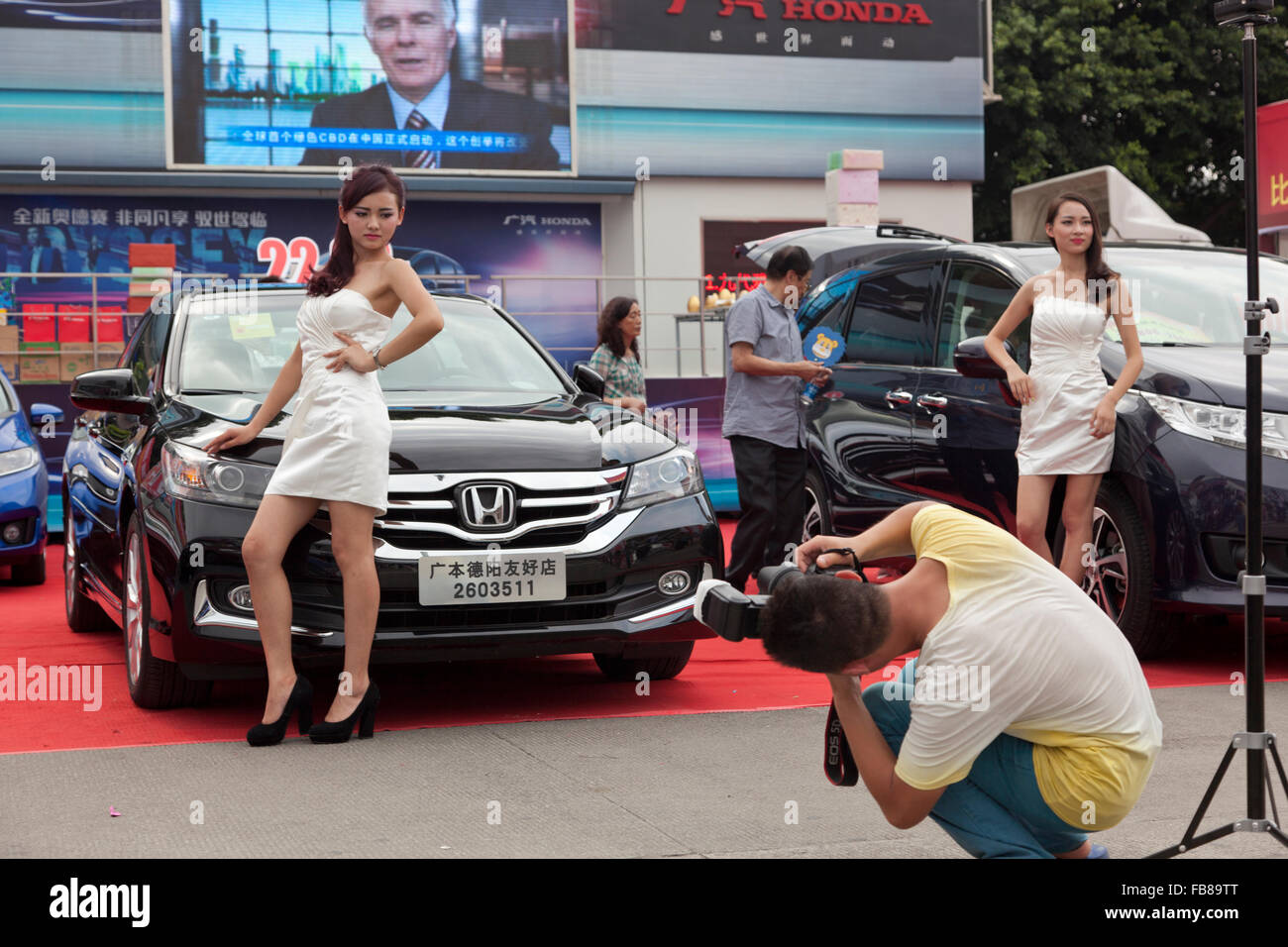 Models posing with cars at a trade fair in China attract amateur photographers and potential buyers to a motor vehicle stand. Stock Photo