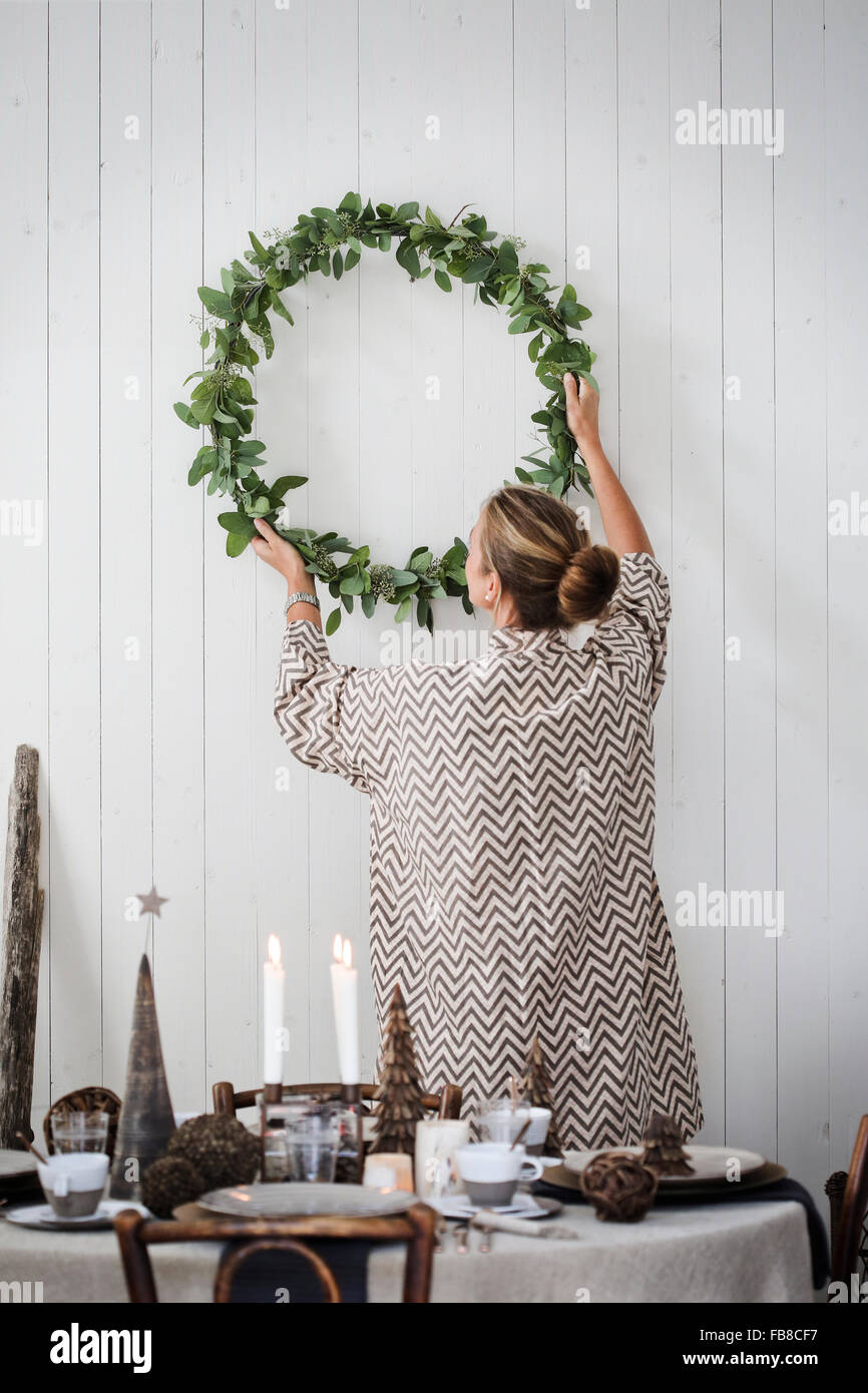 Sweden, Woman hanging Christmas wreath on wall Stock Photo