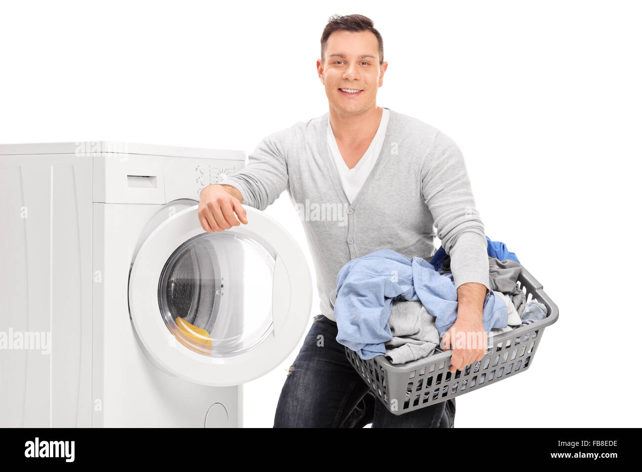 Content young man holding a laundry basket and standing next to a washing machine isolated on white background Stock Photo