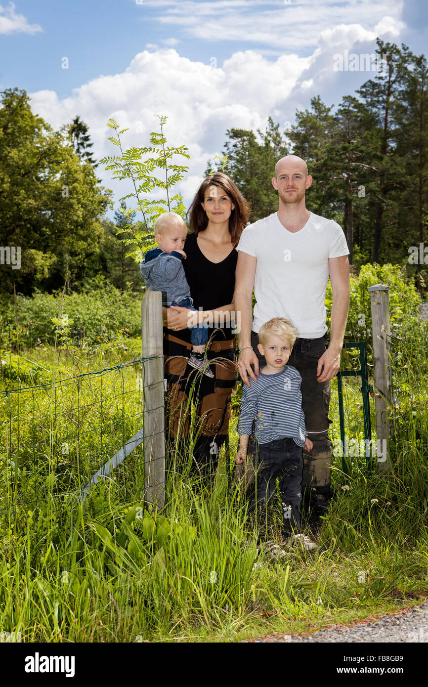 Sweden, Stockholm, Uppland, Nacka, Family with two children (18-23 months, 4-5) standing among lush foliage Stock Photo