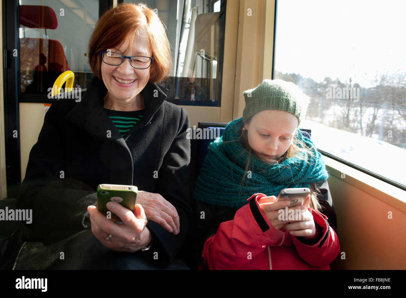Sweden, Stockholm, Girl (10-11) with grandmother sitting in tram and using smart phones Stock Photo