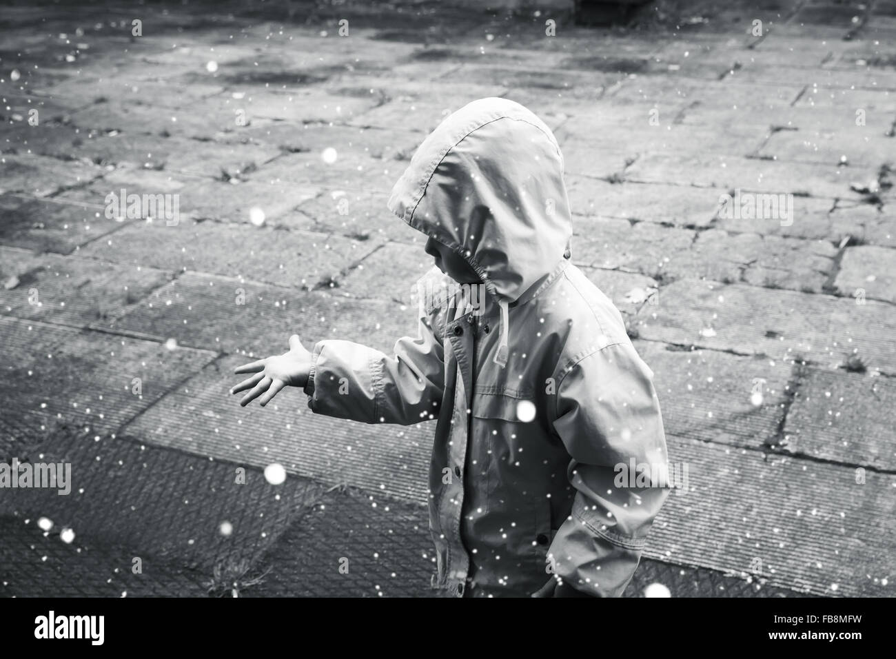 Little child in raincoat playing with raindrops. Monochrome stylized photo Stock Photo