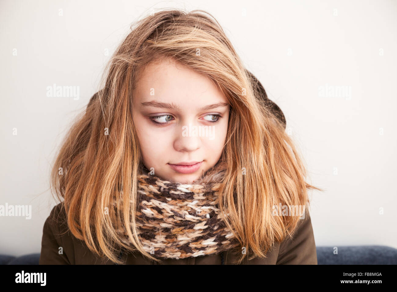 Closeup portrait of beautiful blond Caucasian teenage girl in warm scarf over white wall background Stock Photo