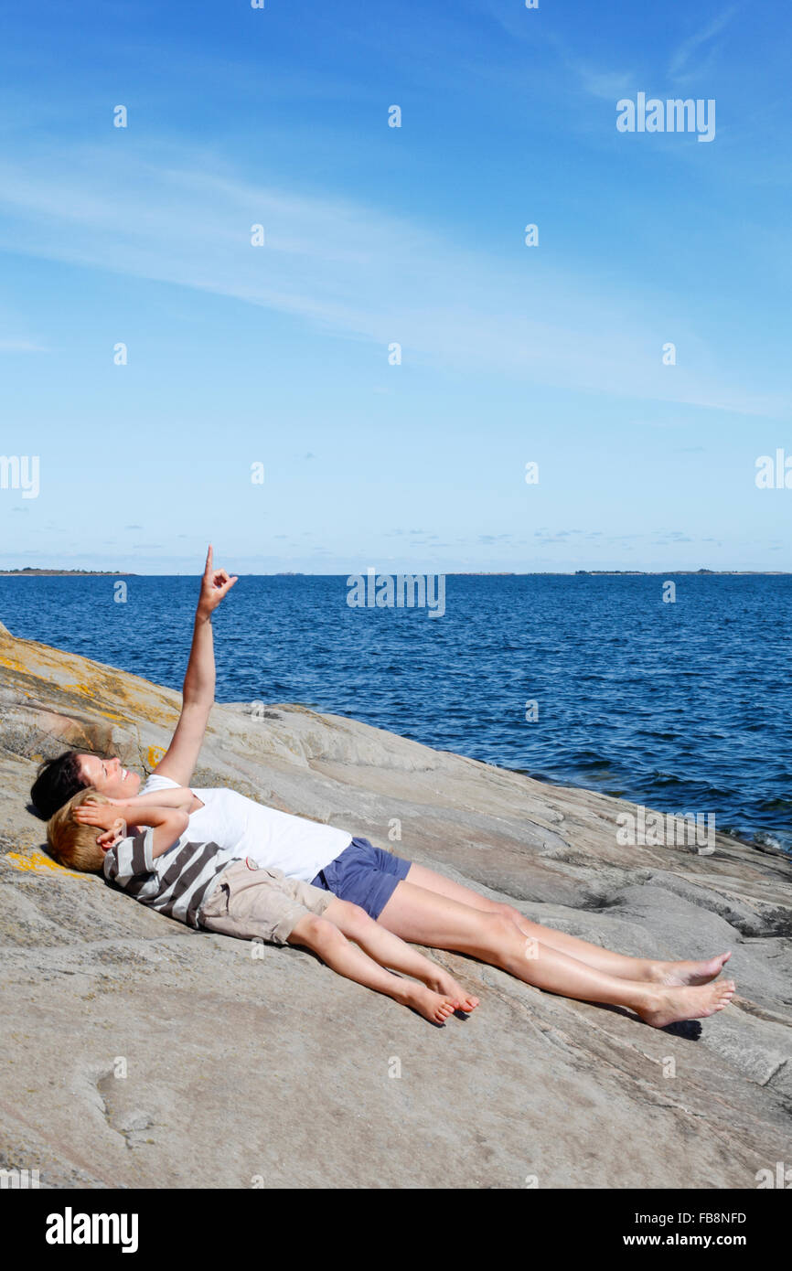Sweden, Uppland, Runmaro, Barrskar, Mother with son (4-5) lying down on seaside Stock Photo