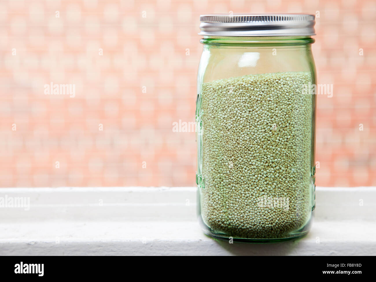 Organic Quinoa in graduated green glass mason jar, on windowsill with brick background. Stock Photo