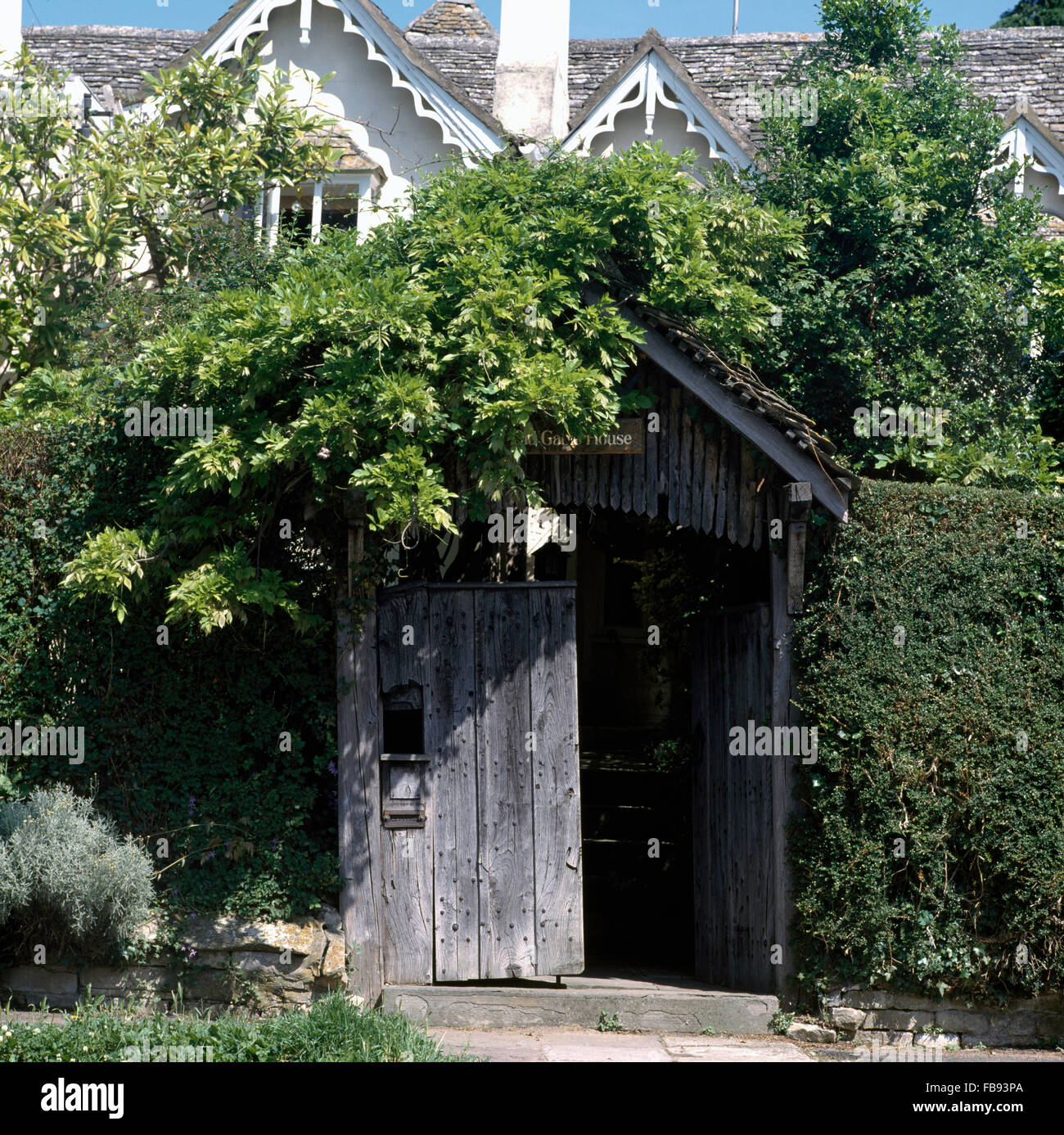 Rustic wooden porch in tall hedge bordering front garden of Victorian country house Stock Photo