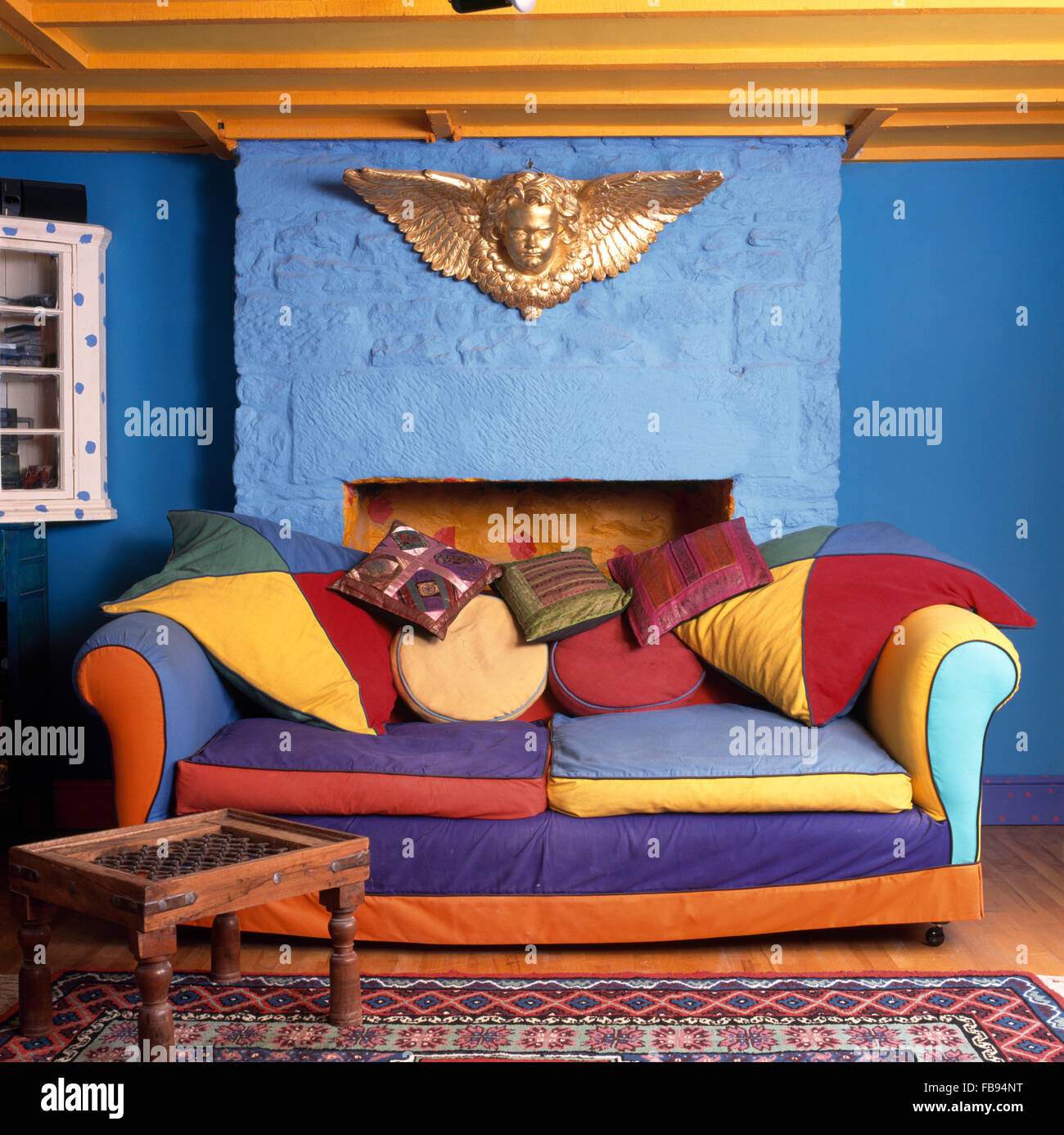Gold cherub above a vibrant, multi colored sofa in a bright blue nineties cottage living room Stock Photo