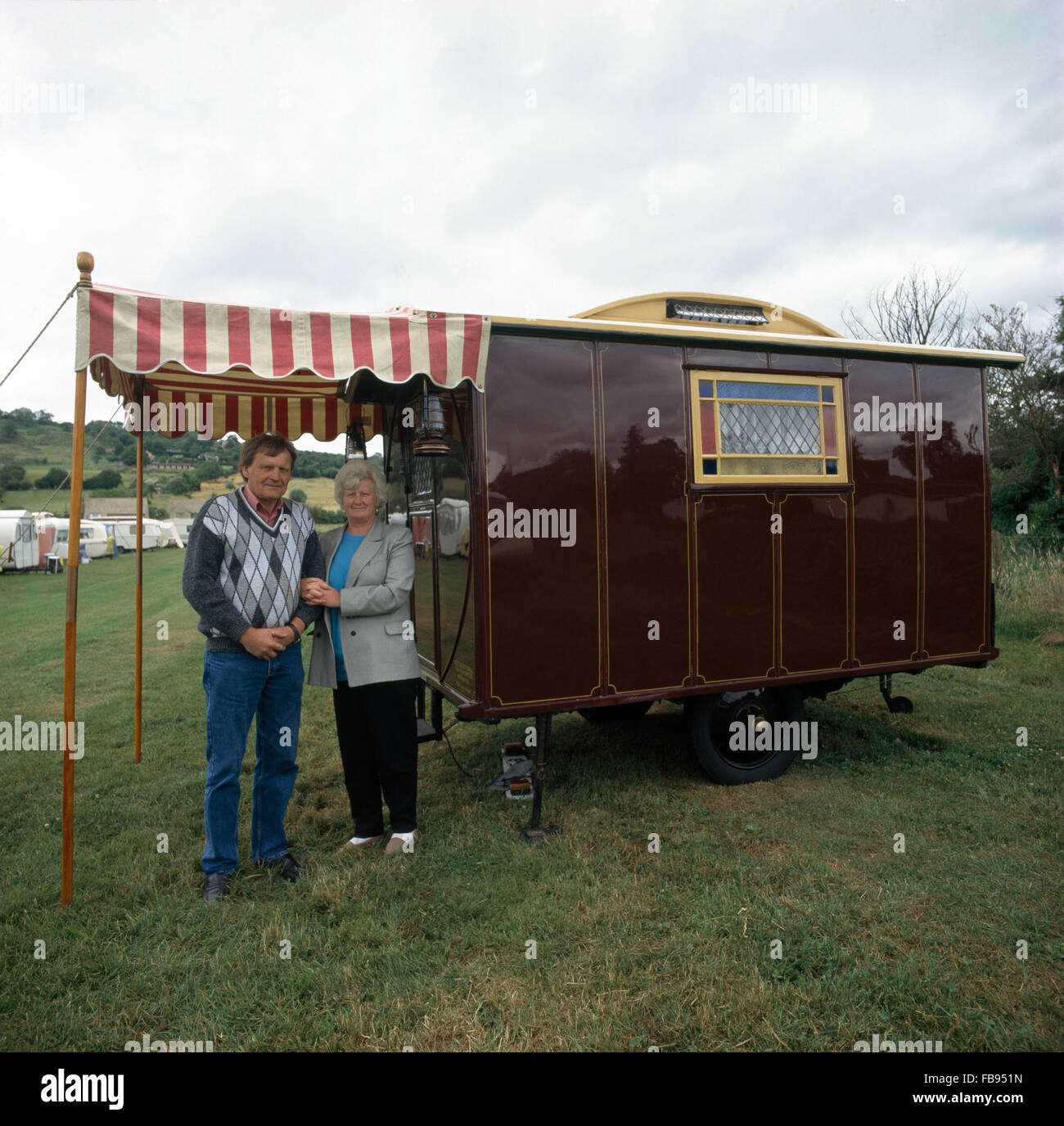 Portrait of a couple standing beside fifties caravan with a striped canvas awning         FOR EDITORIAL USE ONLY Stock Photo