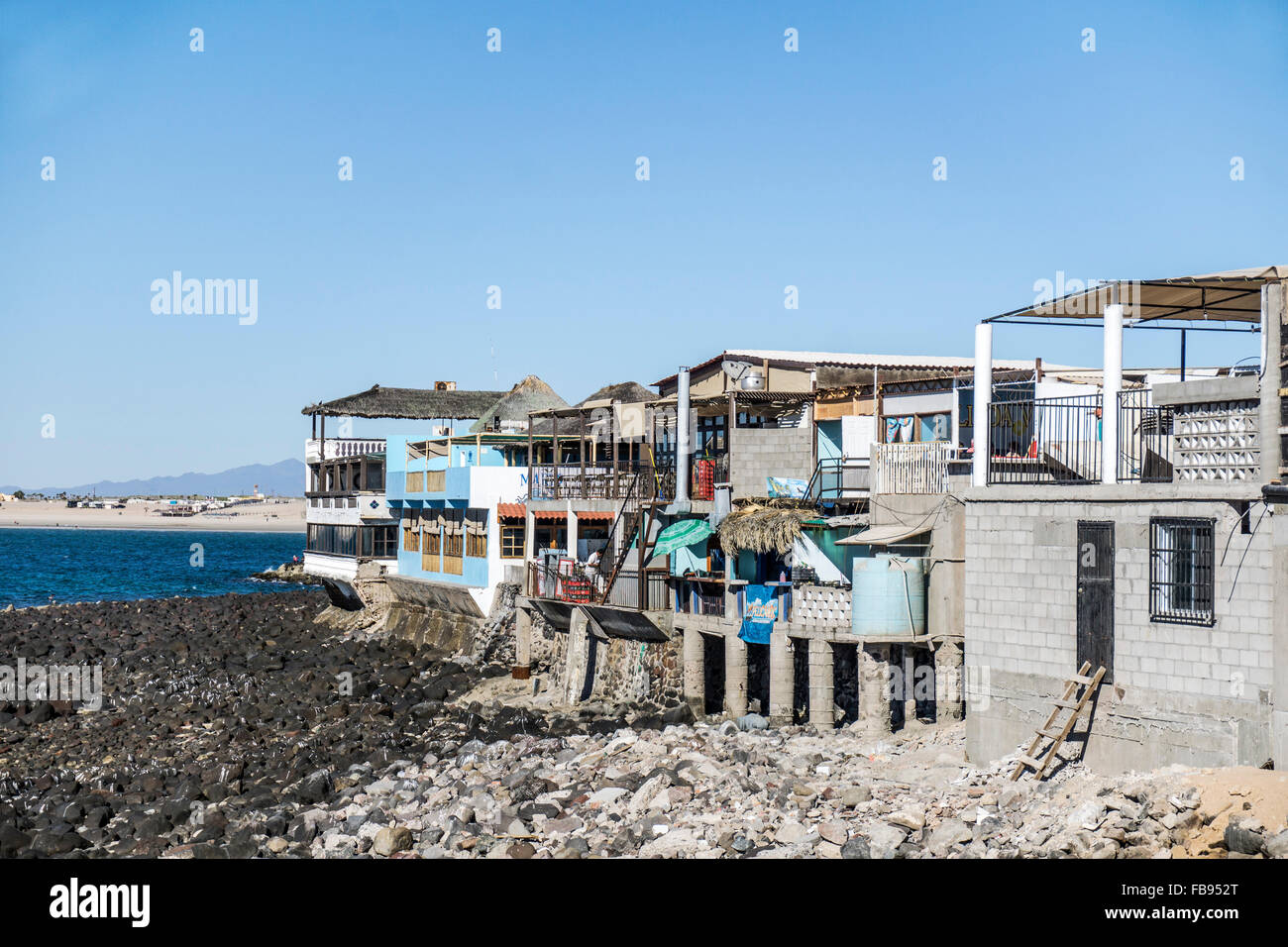 row of disparate restaurants facing Sea of Cortez built up over rocks on concrete seawall or pilings to high water mark Stock Photo