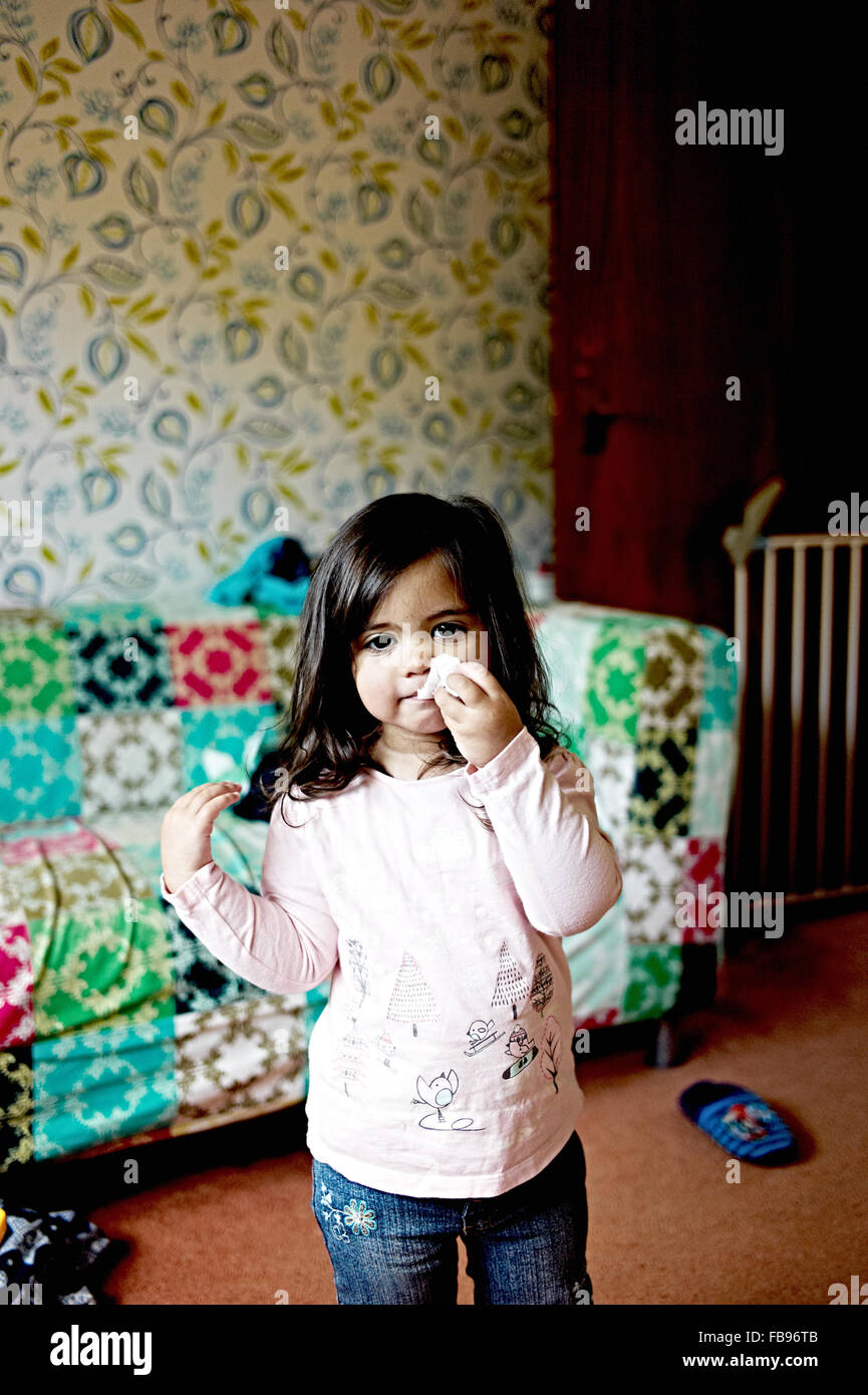 young mixed raced girl wipes her nose with a tissue in the lounge Stock Photo