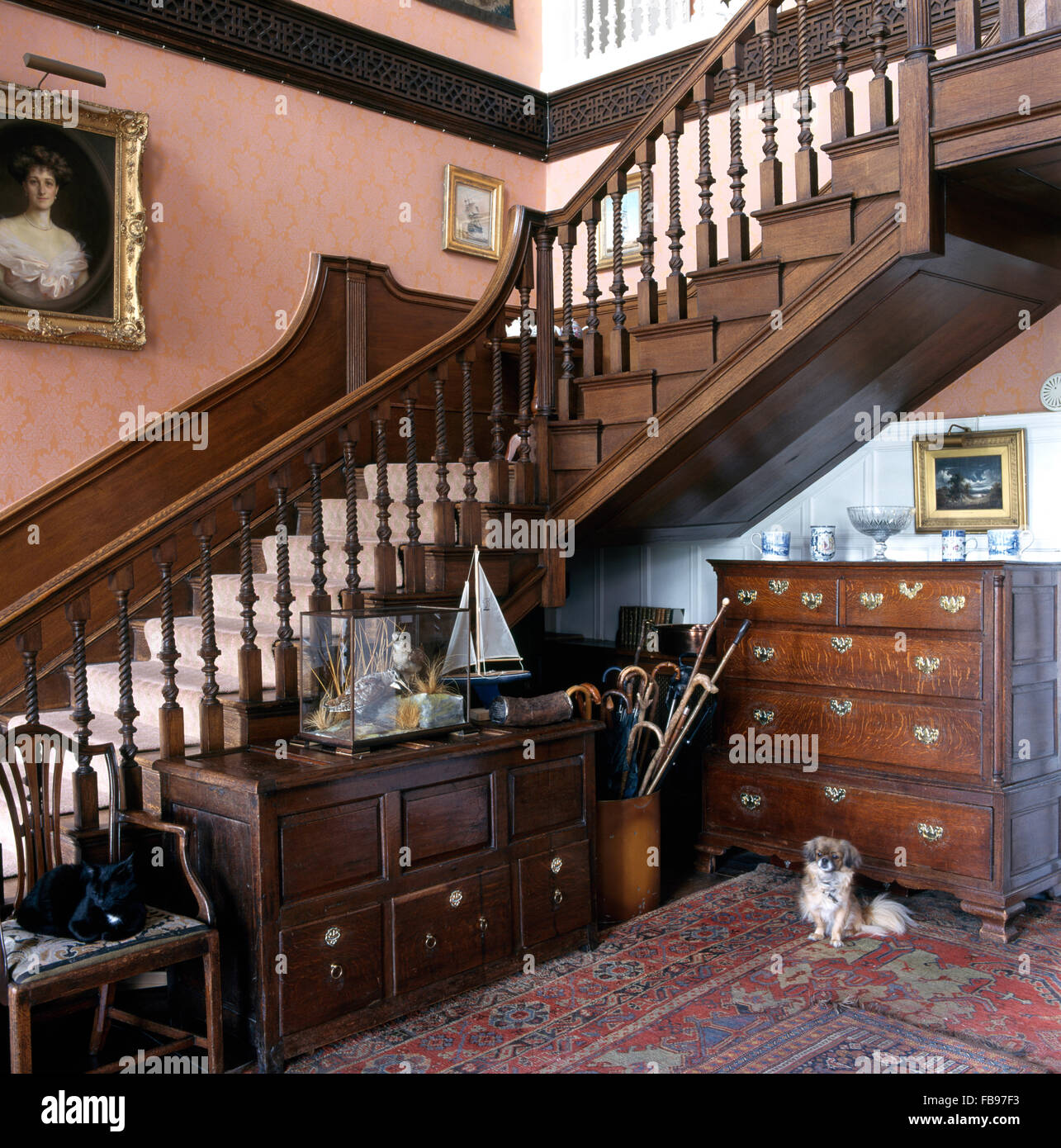 Antique chests-of-drawers below staircase in a large, deep pink Georgian country hall Stock Photo