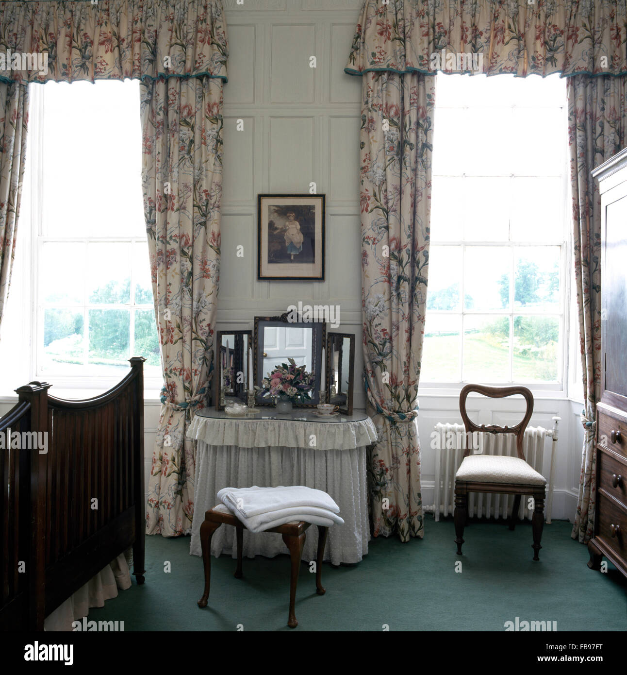 Kidney shaped dressing table with white drapes between tall windows
