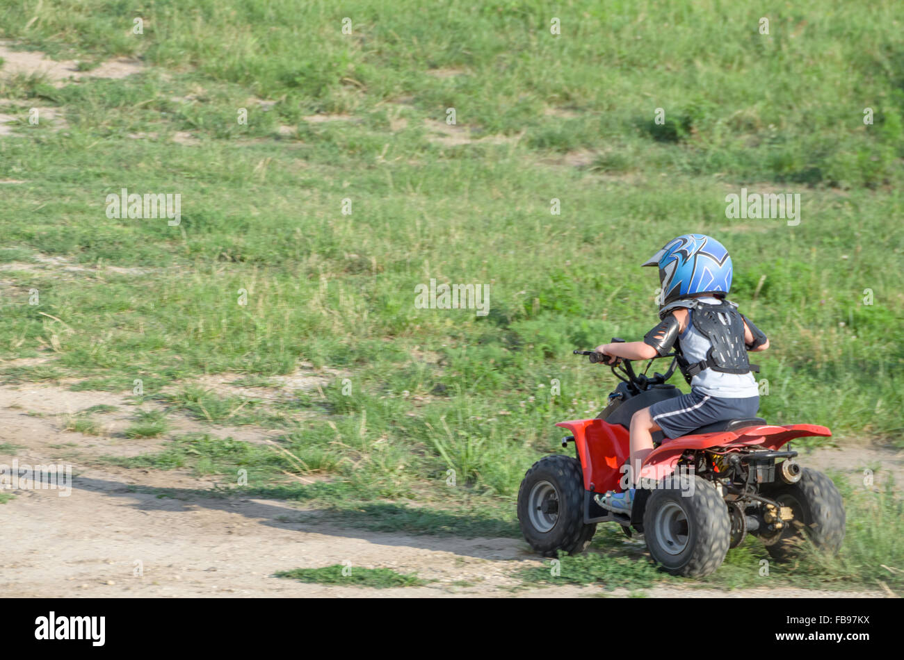 Boy Riding a Red ATV Quad Bike on a Dry Dirt Road on a Summer Day Stock