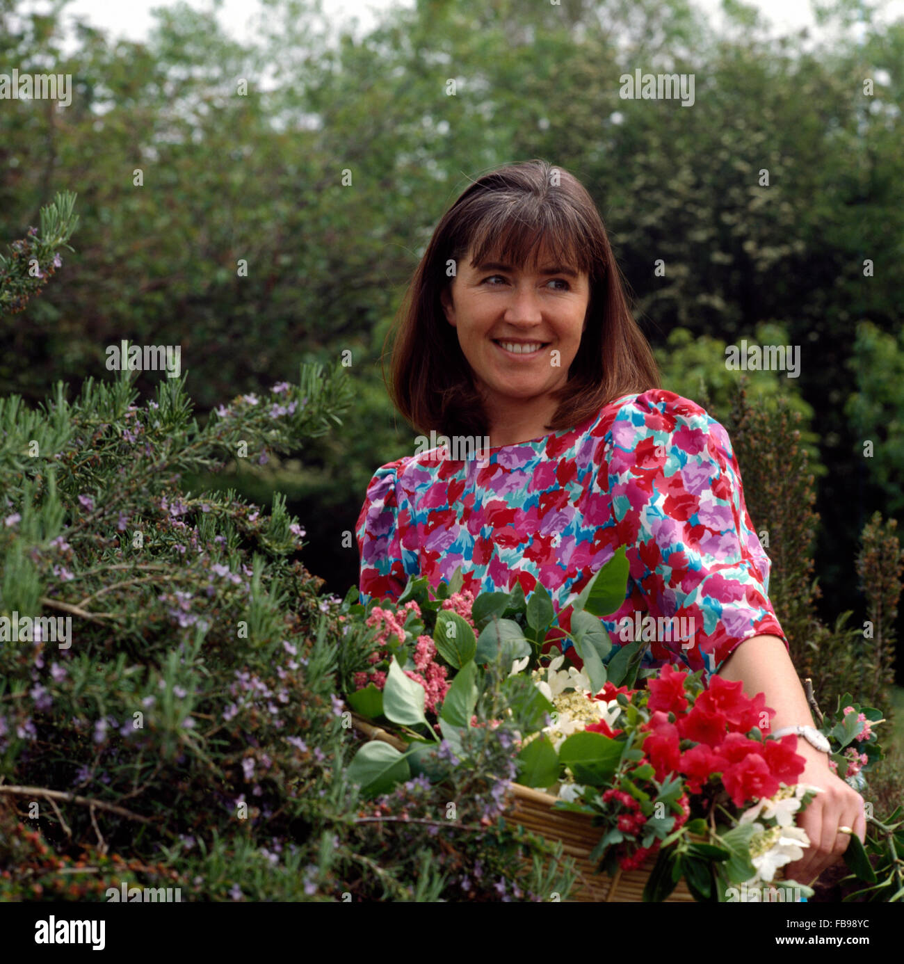 Close-up of a smiling young woman wearing a floral dress and cutting flowers in a garden Stock Photo
