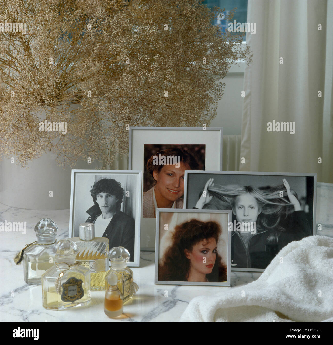 Framed photographs and bottles of perfume on a table with a vase of dried flowers Stock Photo