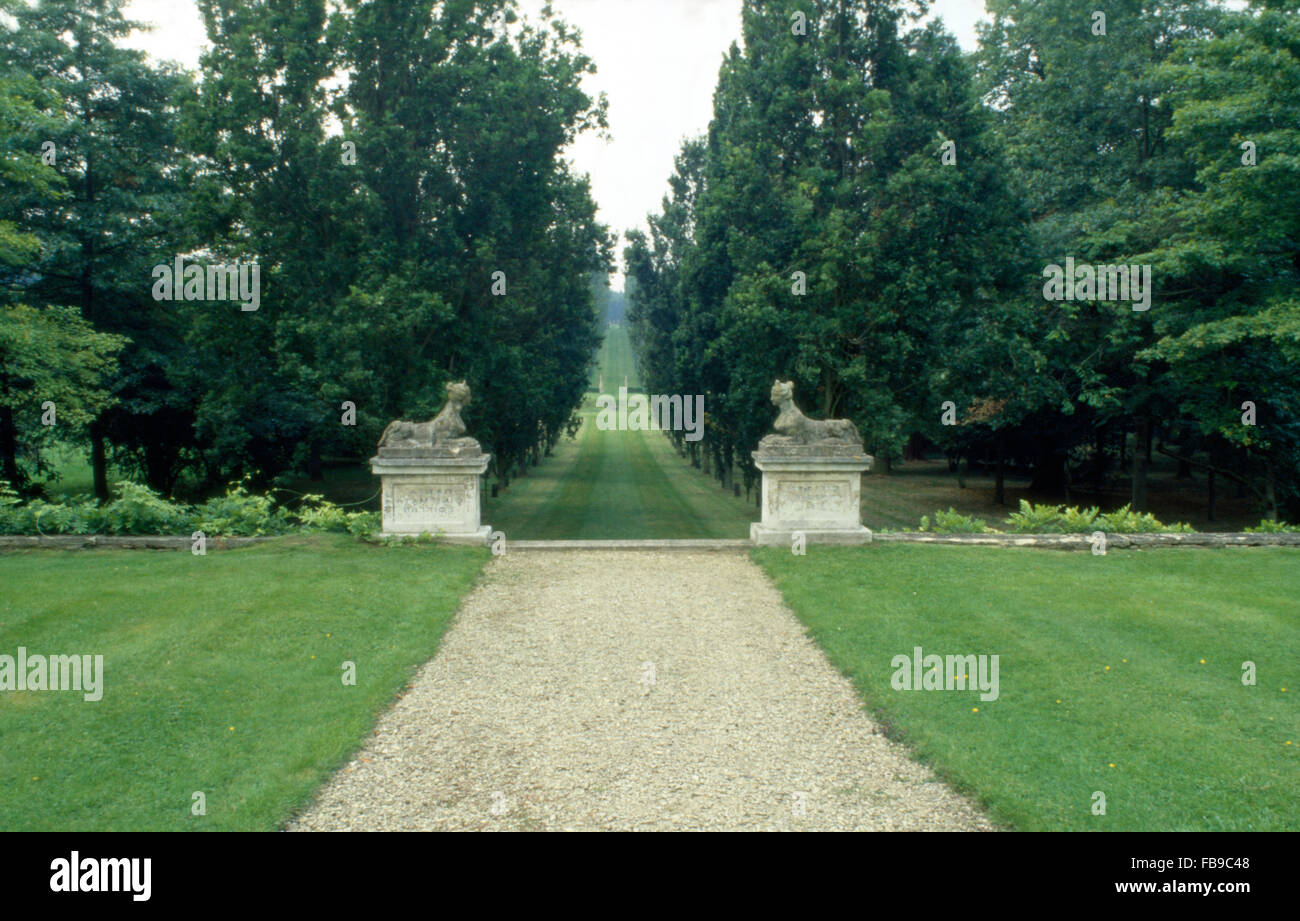 Lawns on either side of gravel path in a large country garden with stone statues on plinths in front of a long avenue Stock Photo