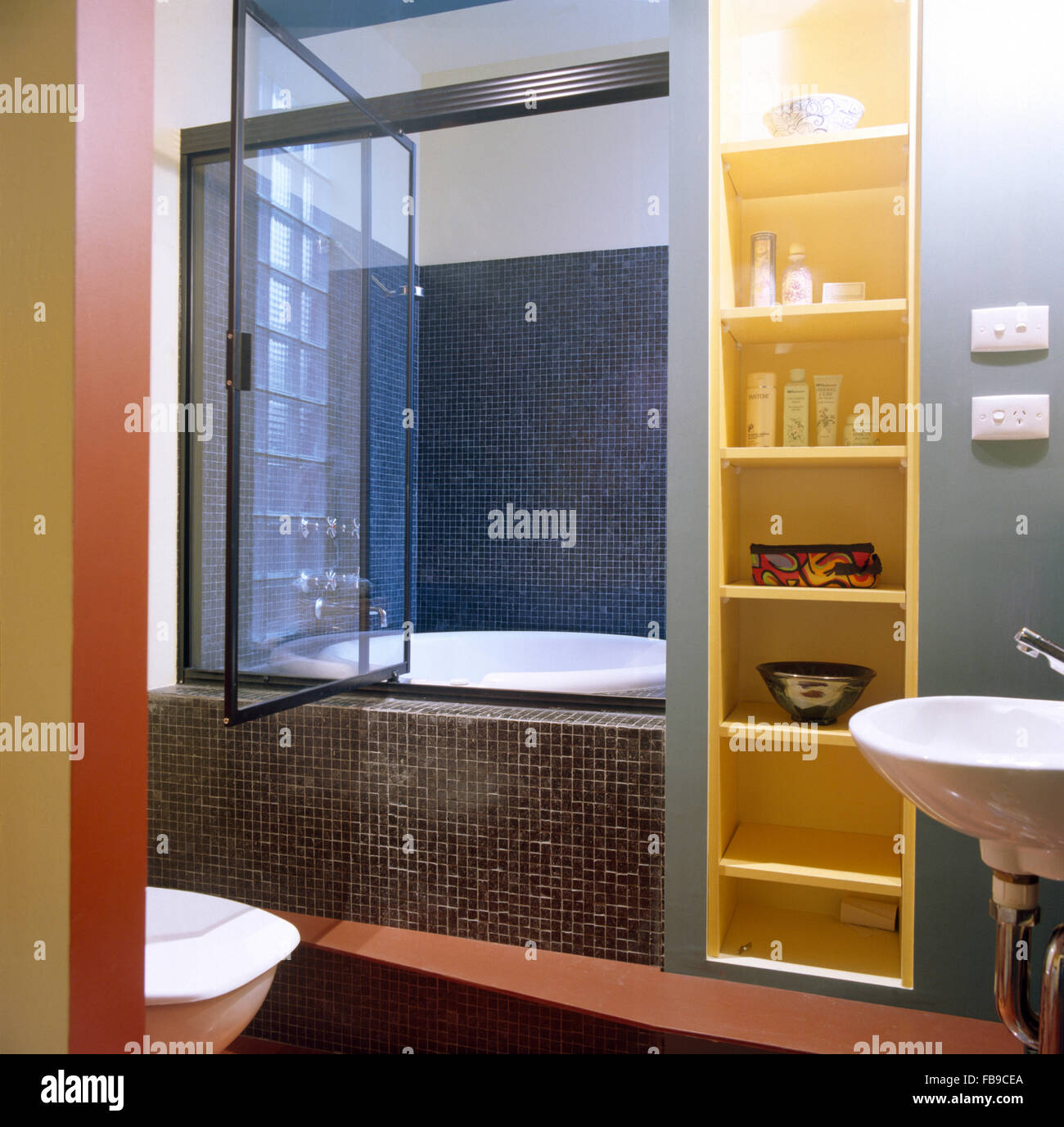 Narrow Shelving Beside Bath With A Glass Shower Door And Gray Mosaic Tiles In A Nineties Bathroom Stock Photo Alamy