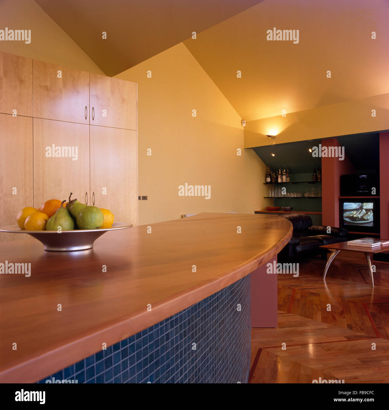 Architectural open-plan  kitchen  with a bowl of fruit on mosaic tiled peninsular unit with a wooden worktop Stock Photo
