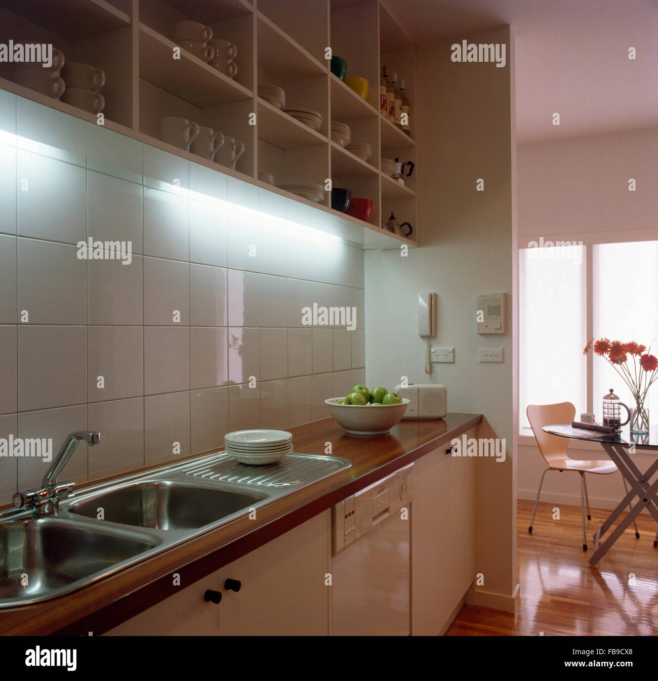 Down lighting above double stainless steel sinks in modern kitchen with open shelving Stock Photo