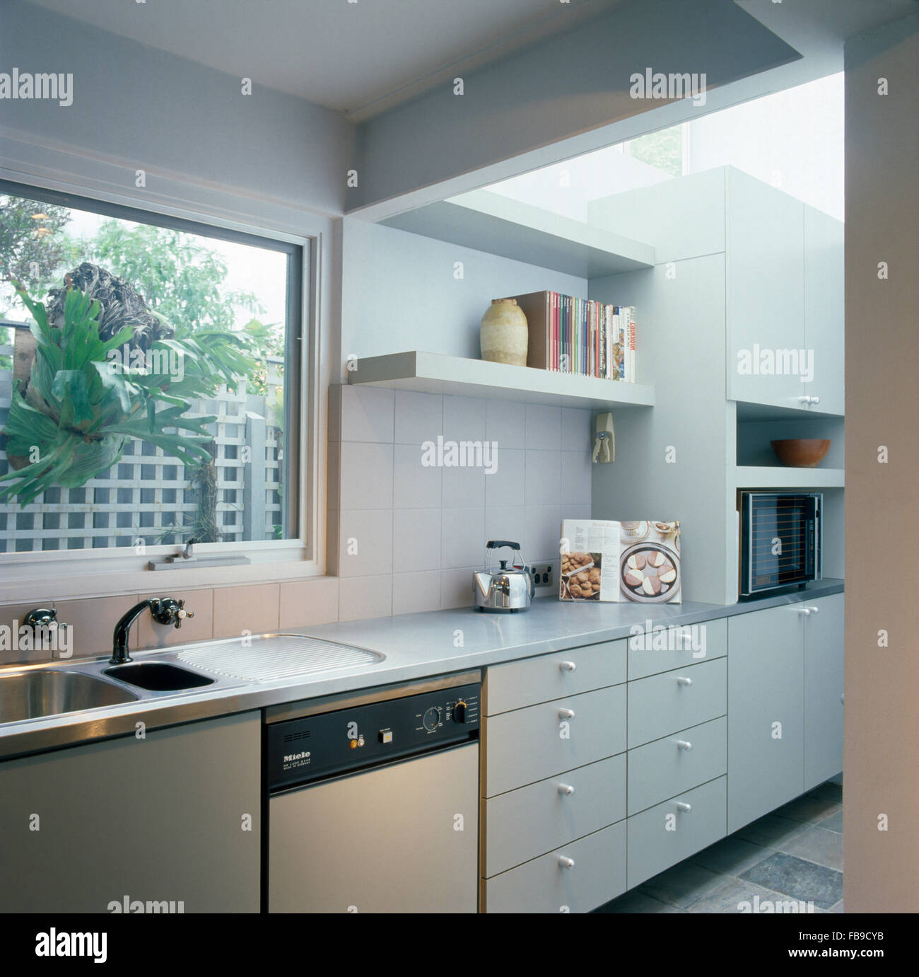 Stainless steel sink and fitted dishwasher below window in nineties kitchen extension Stock Photo