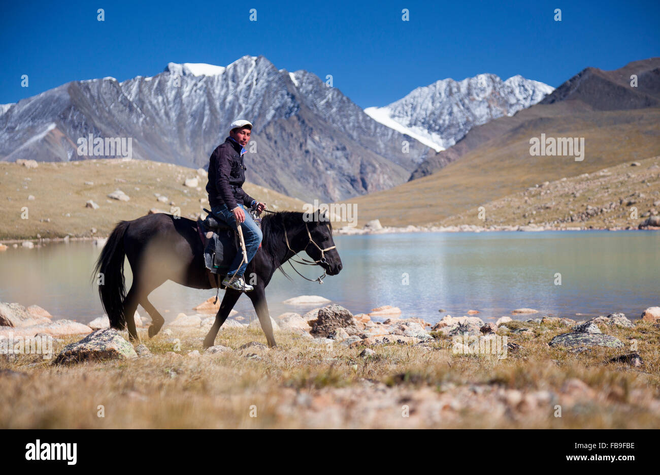 Tsaganaa, a guide and herder riding near a glacial lake in the remote Kharkhiraa Turgen National Park, Mongolia. Stock Photo