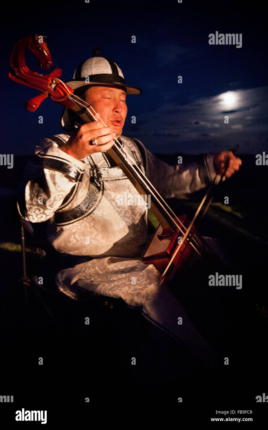 A horse hair fiddler and throat singer conveys the rhythms of horses and steppe life in the moonlight, Mongolia. Stock Photo