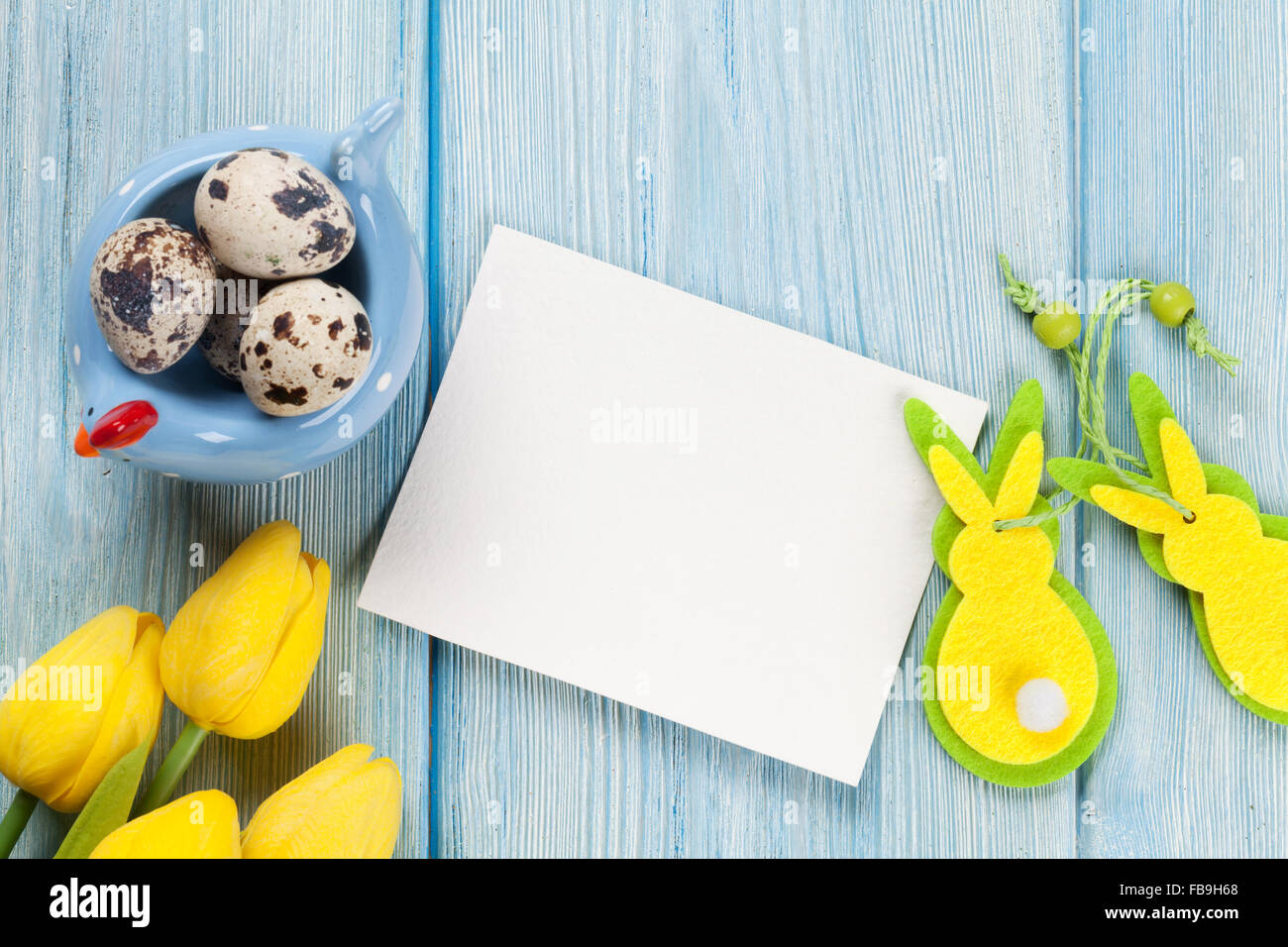 Easter greeting card with eggs and yellow tulips over blue wooden table ...