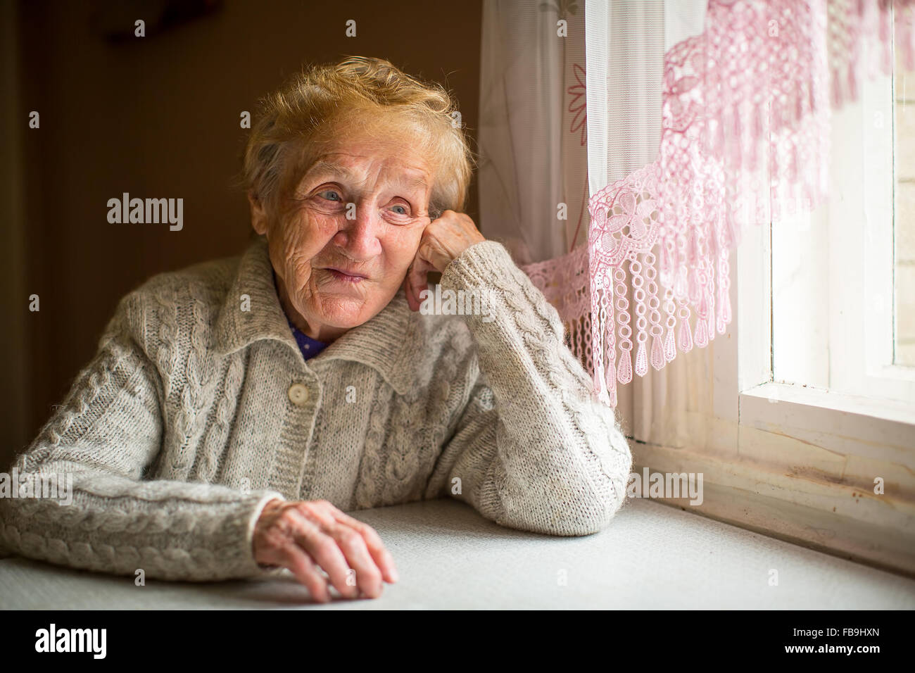 An elderly woman sits near the window in house. Stock Photo