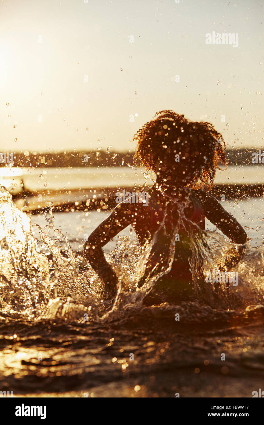 Sweden, Vastra Gotaland, Skagern, Girl (6-7) splashing in lake at sunset Stock Photo