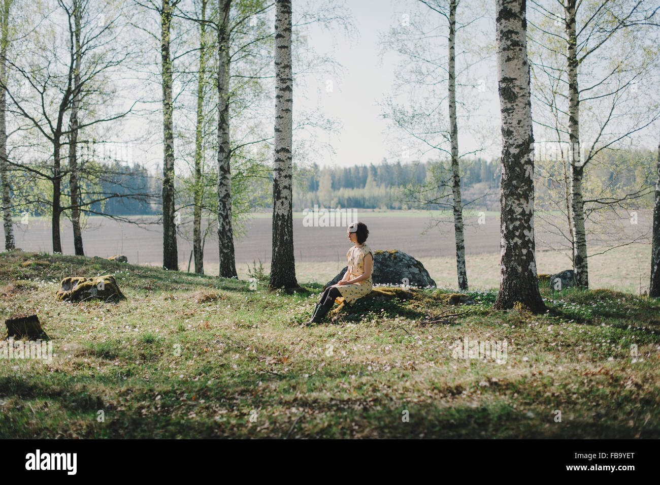 Sweden, Sodermanland, Vingaker, Attersta, Young woman sitting on stump in forest Stock Photo