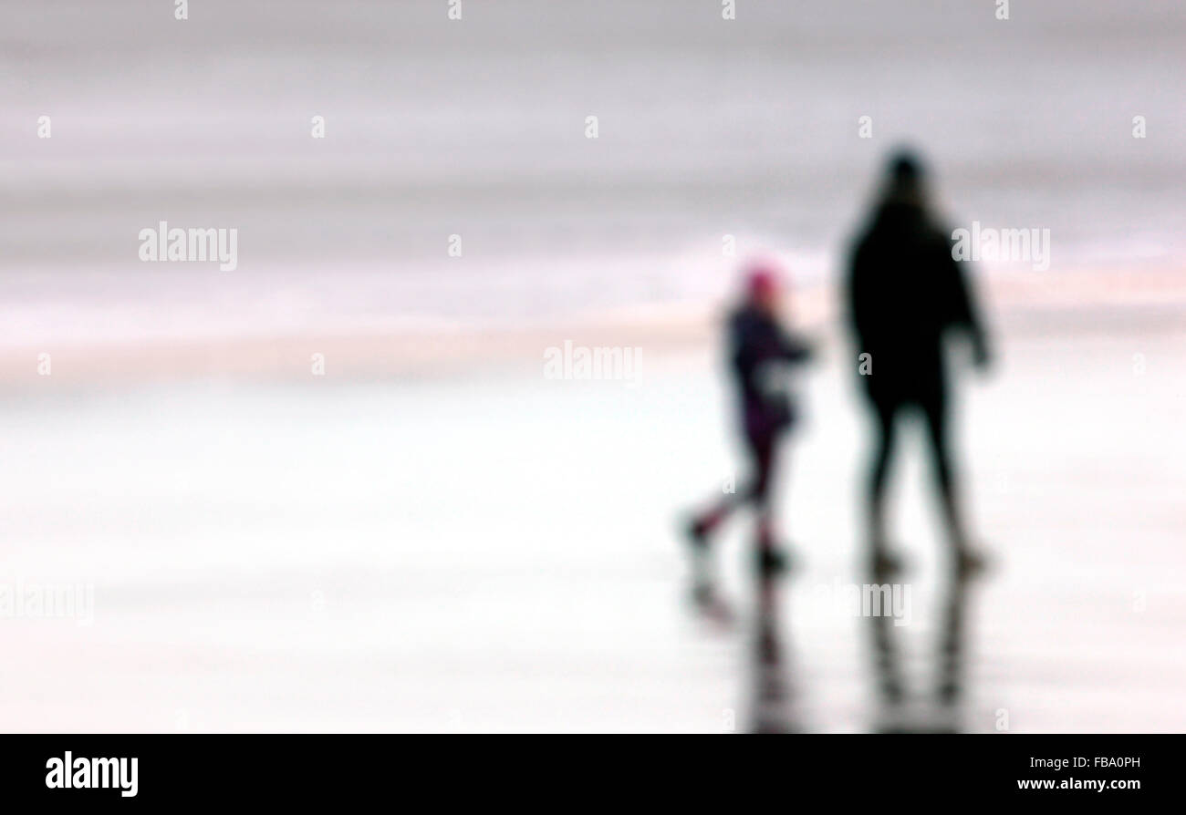Man and boy pictured (deliberately out of focus) walking on a beach Stock Photo