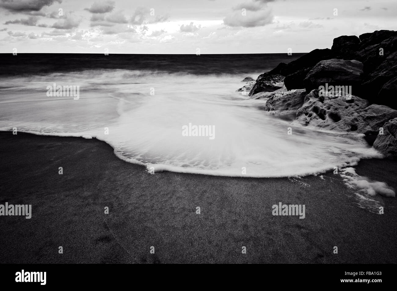 Black and white coastal beach scene with surf and breakwater Stock