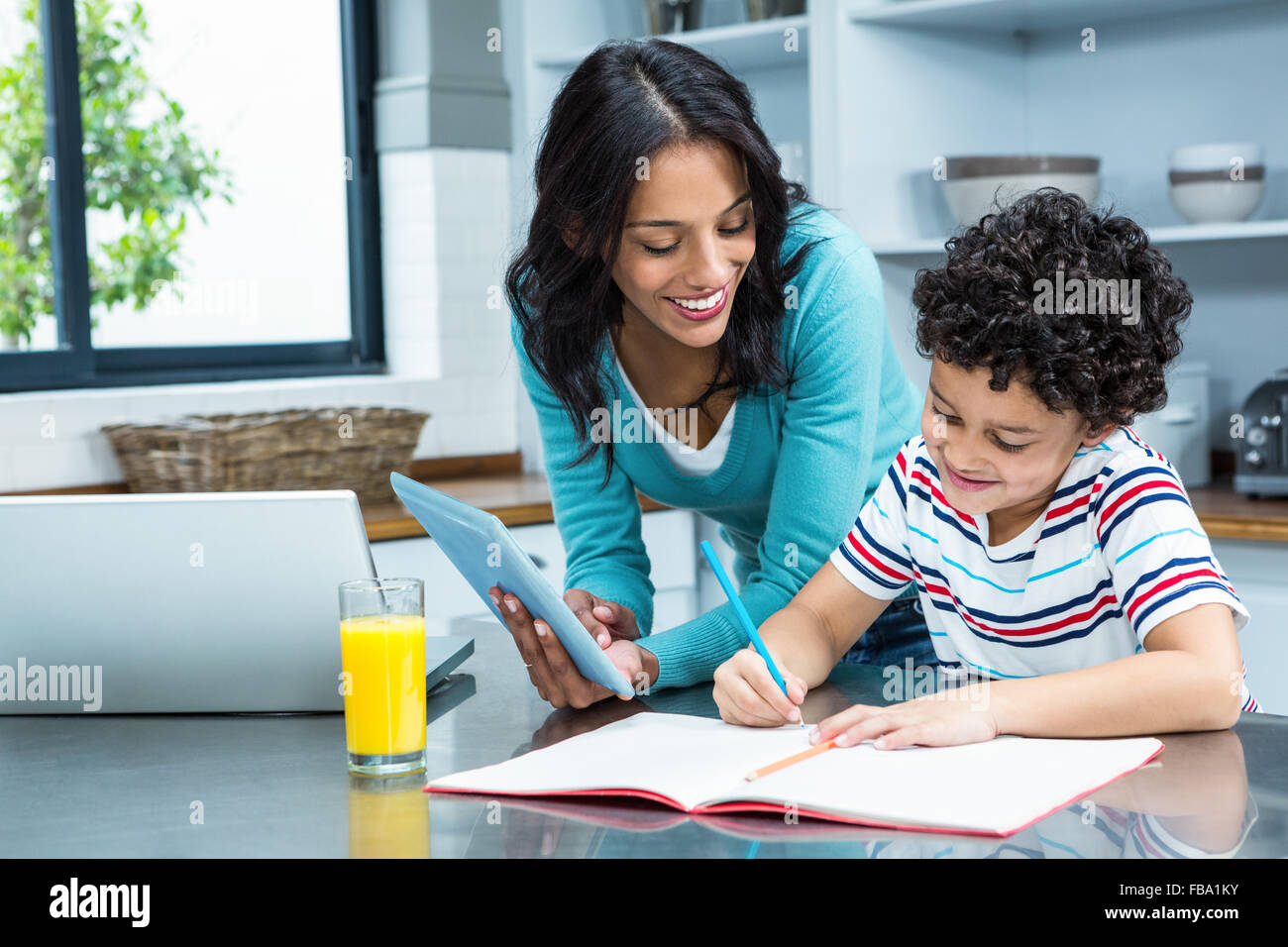 Kind mother helping her son doing homework in kitchen Stock Photo