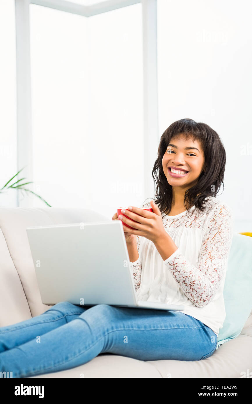 Smiling woman relaxing on couch with coffee using laptop Stock Photo ...