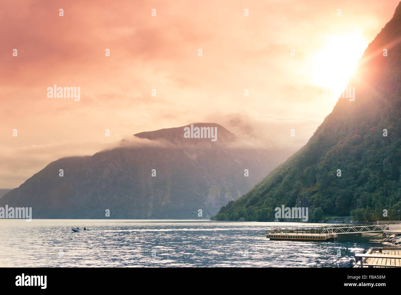 Norway, More og Romsdal, Sunnmore, Geirangerfjord, Sun setting behind mountains over calm harbor Stock Photo