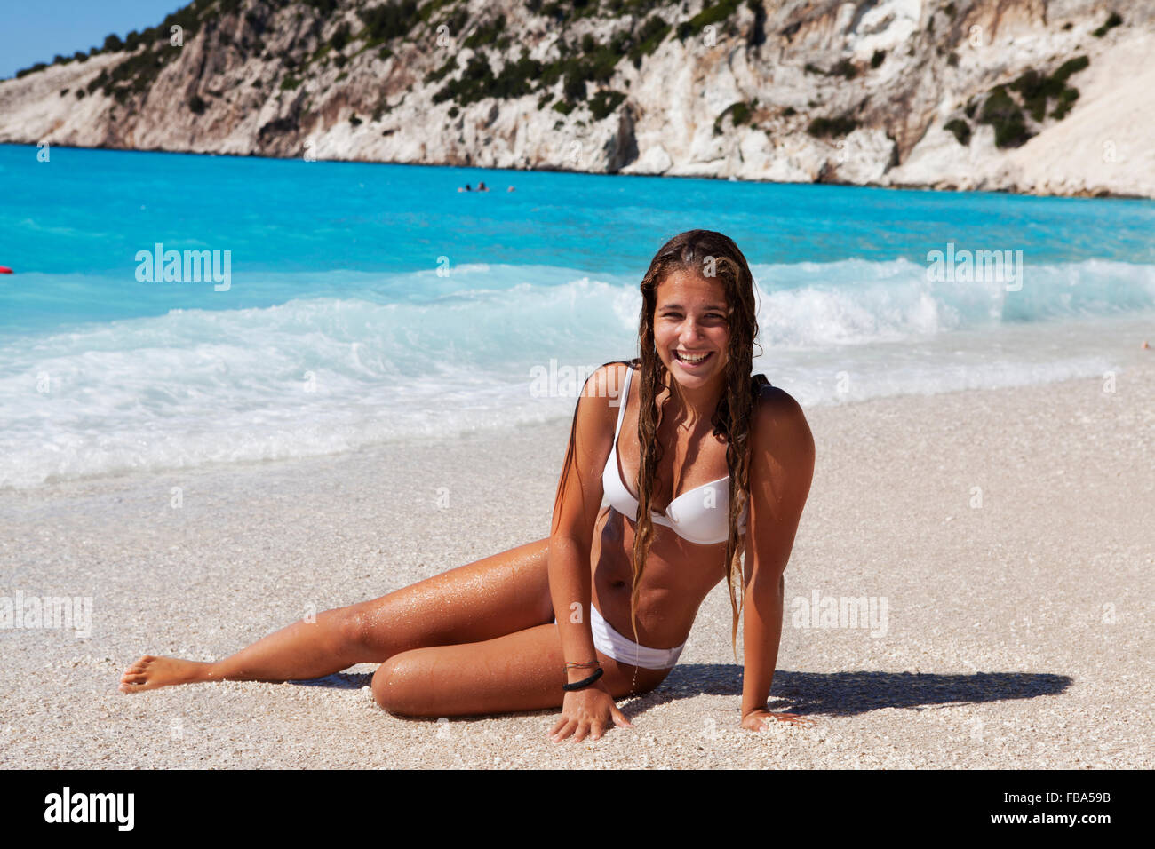 young girl sittingon a white pebble beach with the ocean behind. Myrtos Beach, Kefalonia island, Greece Stock Photo