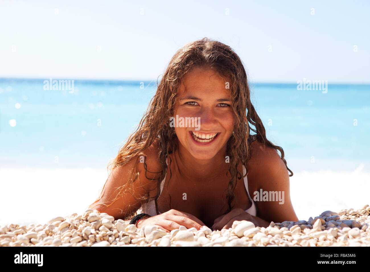 young girl laying on a white pebble beach with the ocean behind. Myrtos Beach, Kefalonia island, Greece Stock Photo