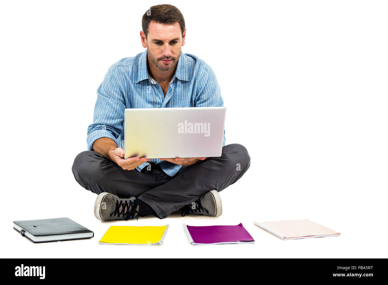 Man sitting on floor using laptop with notepads on floor Stock Photo