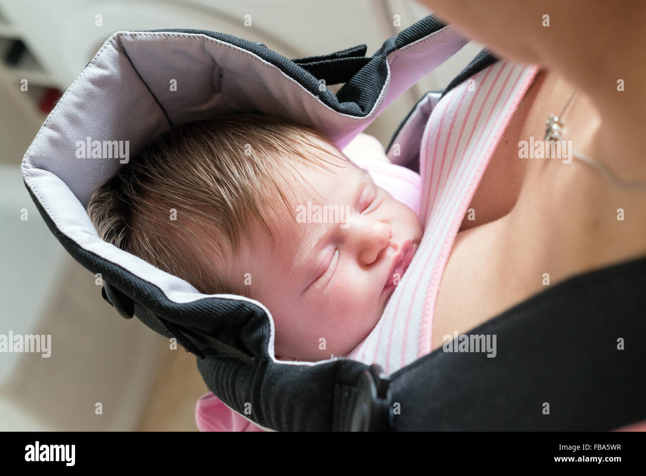 Mother carrying her sleeping newborn baby in a sling Stock Photo