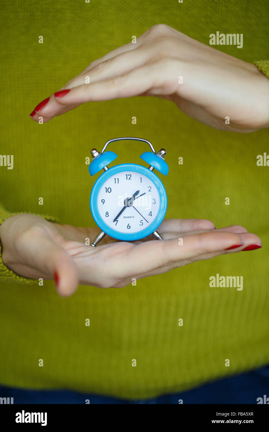 Little blue alarm clock in the hands of women, the concept of saving