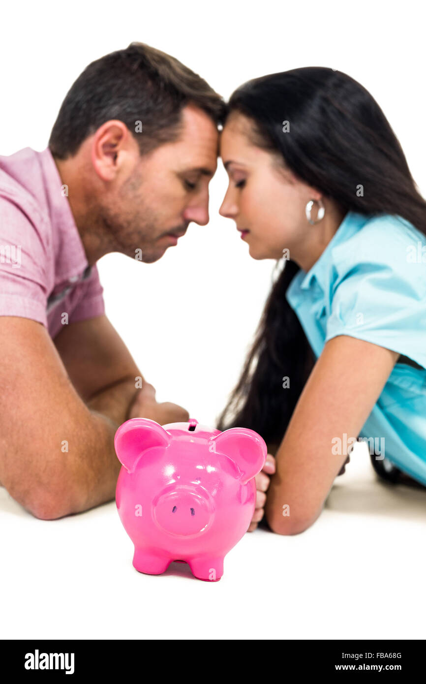 Worried couple laying on the floor face to face with piggybank Stock Photo