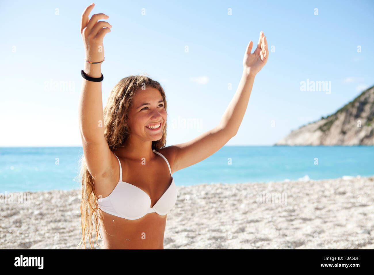 Young blond girl smiling open arms on a white beach wearing white bikini. Myrtos beach Lixouri, Kefalonia, Ionian Islands Greece Stock Photo