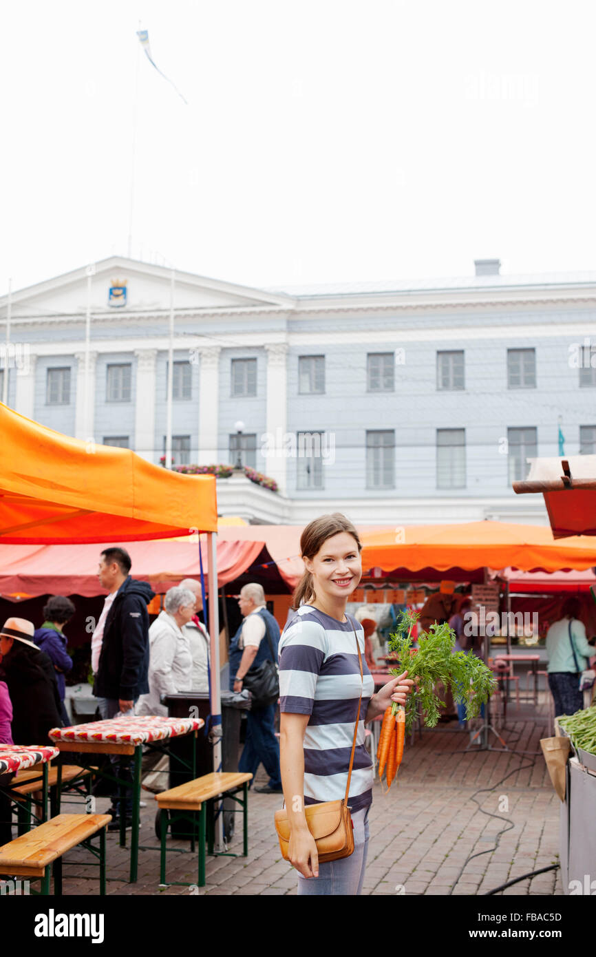 Finland, Uusimaa, Helsinki, Kauppatori, Smiling woman holding carrot at street market Stock Photo