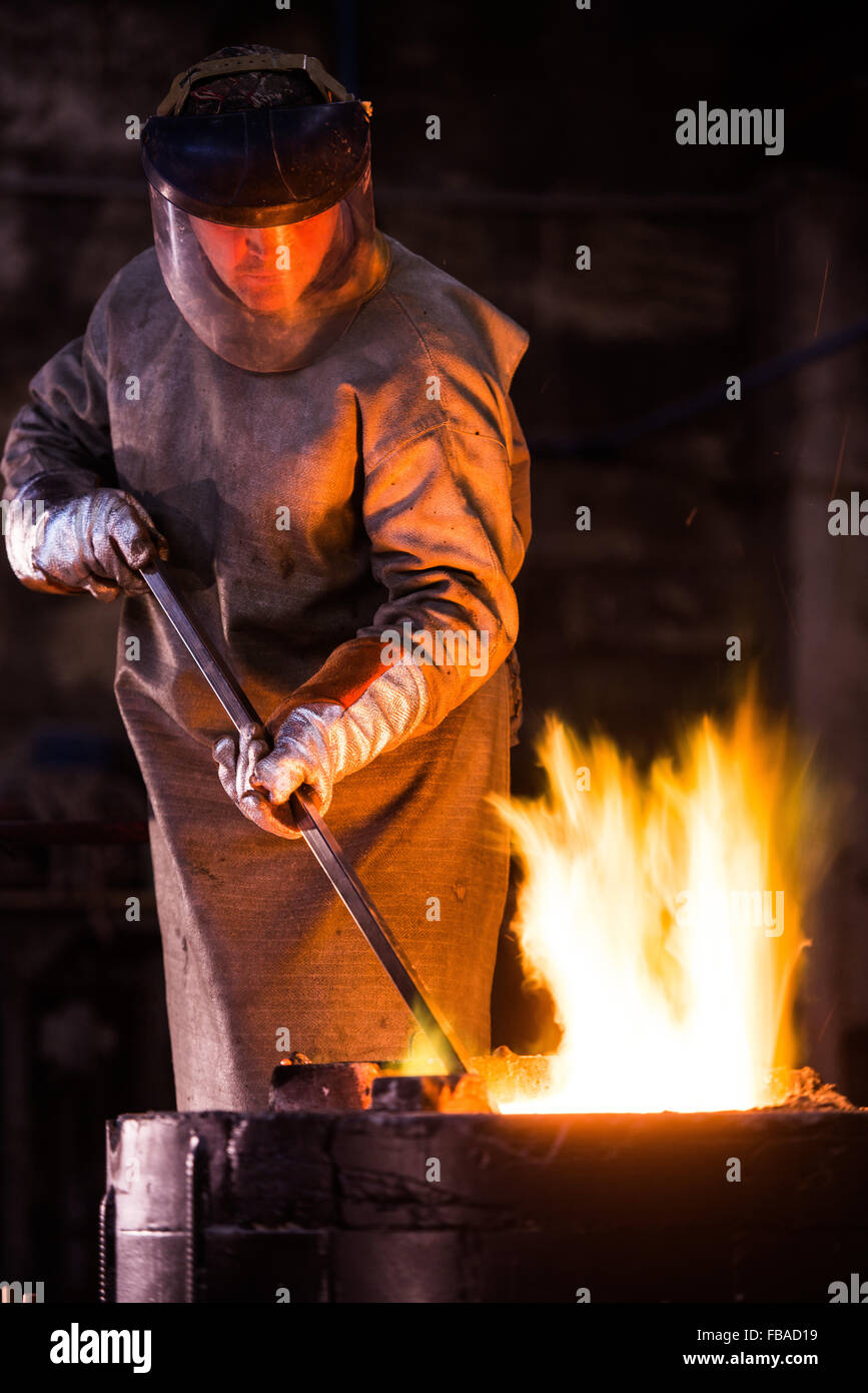 Steel worker in protective clothing raking furnace in an industrial foundry Stock Photo