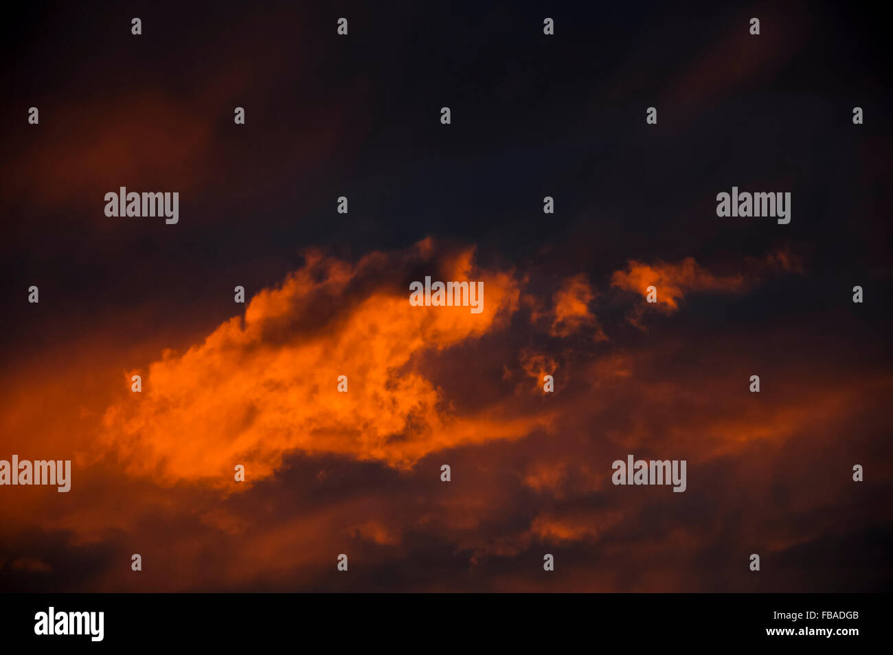 Deep orange glow on floating clouds at sunset. Stock Photo